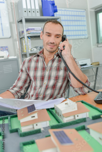 Man on telephone, model houses in front of him
