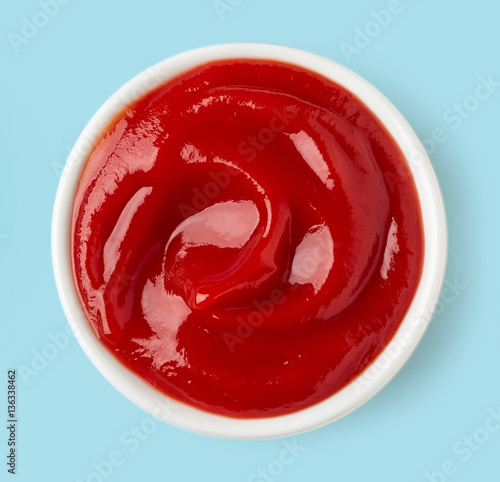 Bowl of ketchup on blue background, from above