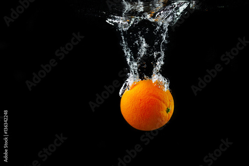 Fresh orange falling into the water with a splash and air bubbles. Healthy food on black background. Wash fruits.
