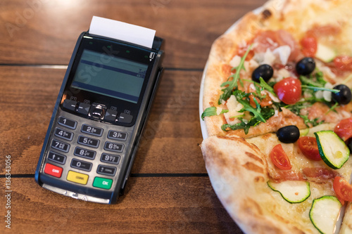 POS machine next to pizza on the wooden table.