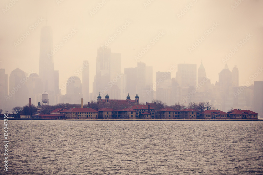 Fototapeta premium Ellis Island against ghostly New York City Skyline on a cloudy day