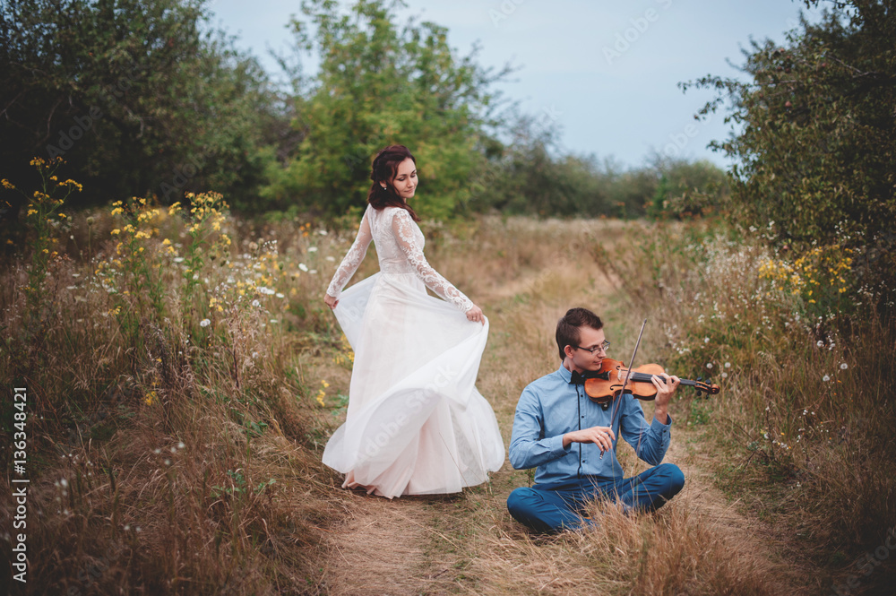 Fototapeta premium Violinist and woman in white dress , young man plays on the violin the background nature,Young hipster musician man playing violin in the nature outdoor lifestyle