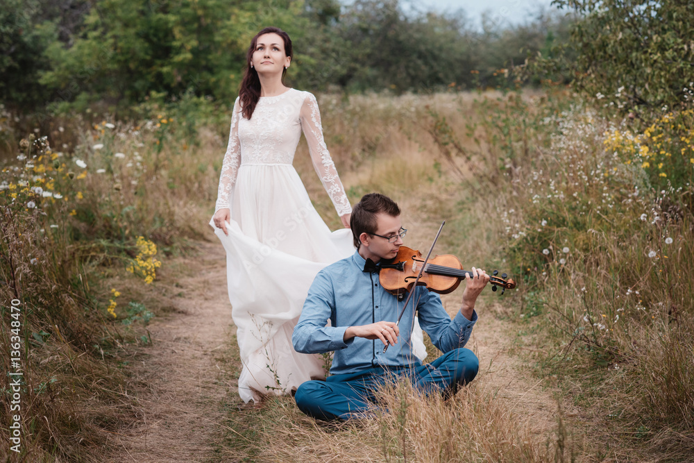 Fototapeta premium Violinist and woman in white dress , young man plays on the violin the background nature,Young hipster musician man playing violin in the nature outdoor lifestyle