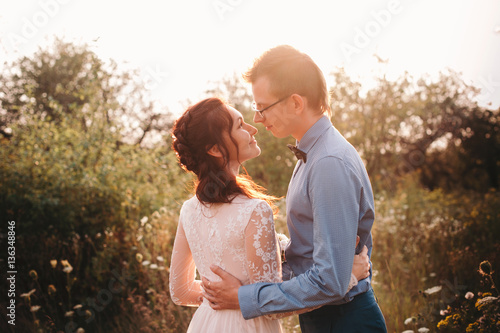 Just married loving hipster couple in wedding dress and suit on a green field in the woods. happy bride and groom walking running and dancing on a summer meadow. Romantic married to a young family