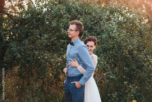 Just married loving hipster couple in wedding dress and suit on a green field in the woods. happy bride and groom walking running and dancing on a summer meadow. Romantic married to a young family