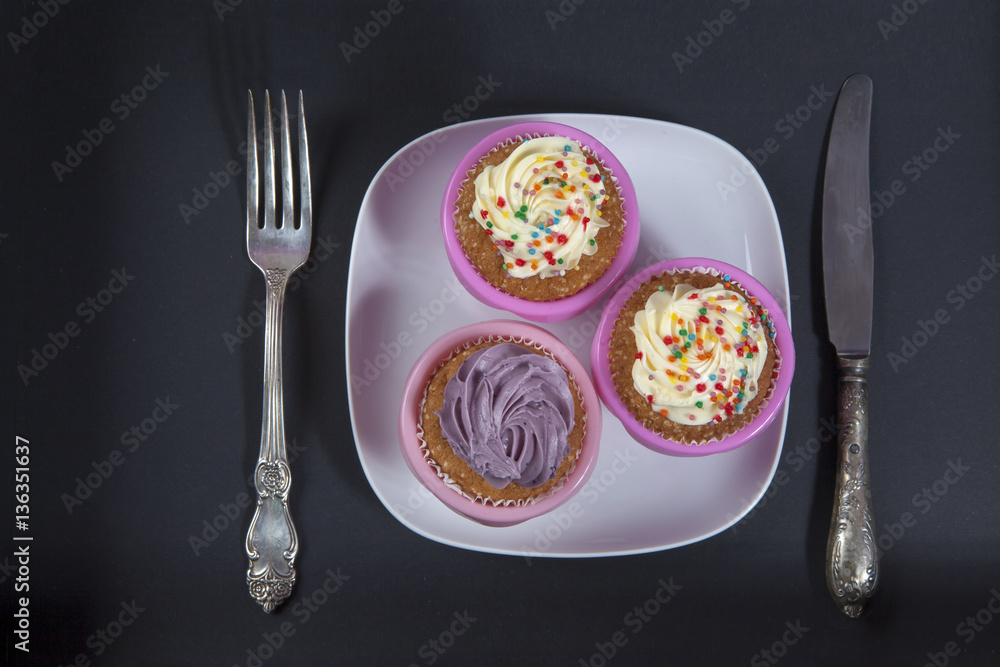 the cupcakes with white and violet cream with fork and knife on the black background, the cupcakes with white and violet cream with fork and knife on the black background,