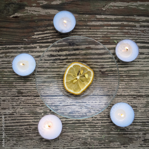The dried lemon is surrounded of candles on wooden table