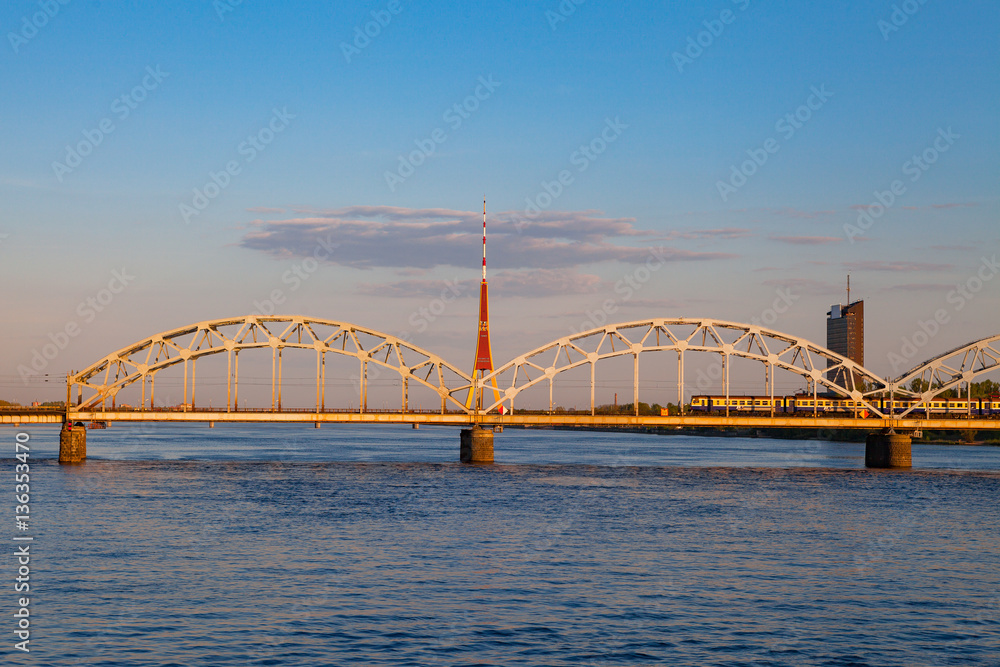 Train is running by the bridge over Daugava. TV tower and sunset time. Riga, Latvia