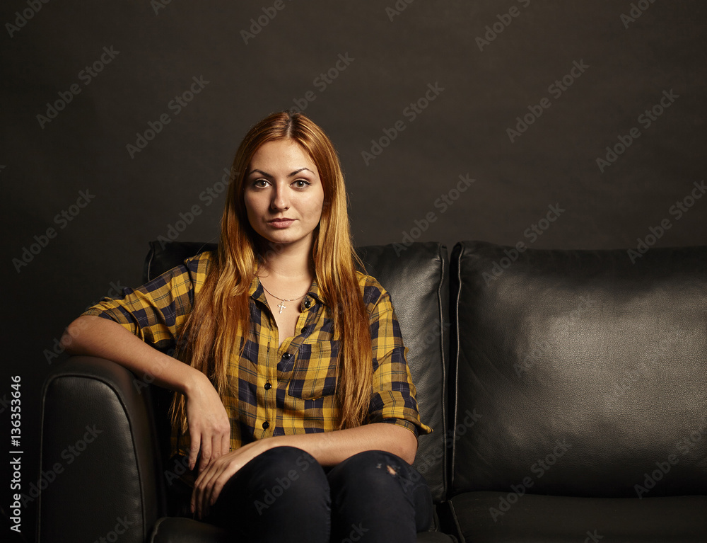 Attractive young woman with red hairs sitting on black sofa on black background Attractive young woman with red hairs sitting on black sofa on black background