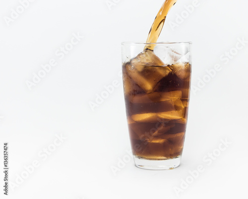 soft drink pouring from a plastic bottle into a glass filled with ice cubes and cola