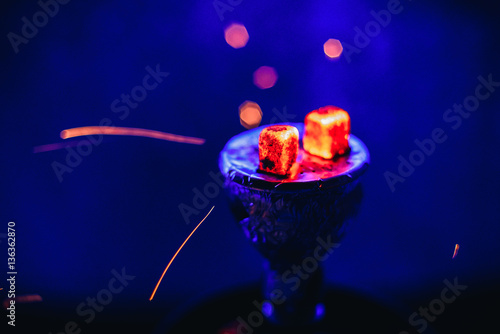 Shisha hookah with glowing red embers and flying sparks in bowl on blue background photo