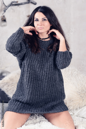 Beautiful sexy tan brunette woman posing in bedroom, wearing cozy grey sweater and knitted socks. Rest, sleeping, comfort concept. Close up of young woman lying in bed at home. Scandinavian home. 