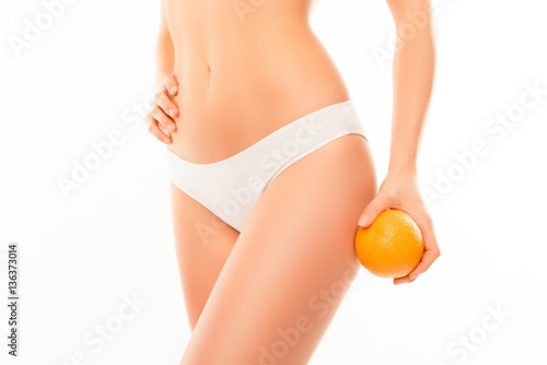 Close up of woman in white pants holding orange near hip
