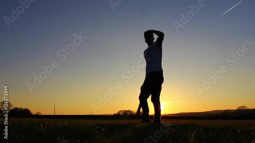 Silhouette of baseball player hitting ball, sunset