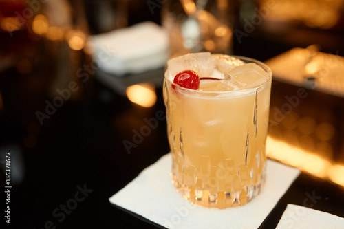 yellow cocktail decorated with cherry on the bar