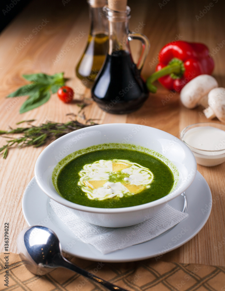 white plate with soup green, poured sour cream on wooden table surrounded by decor white plate with soup green, poured sour cream on wooden table surrounded by decor