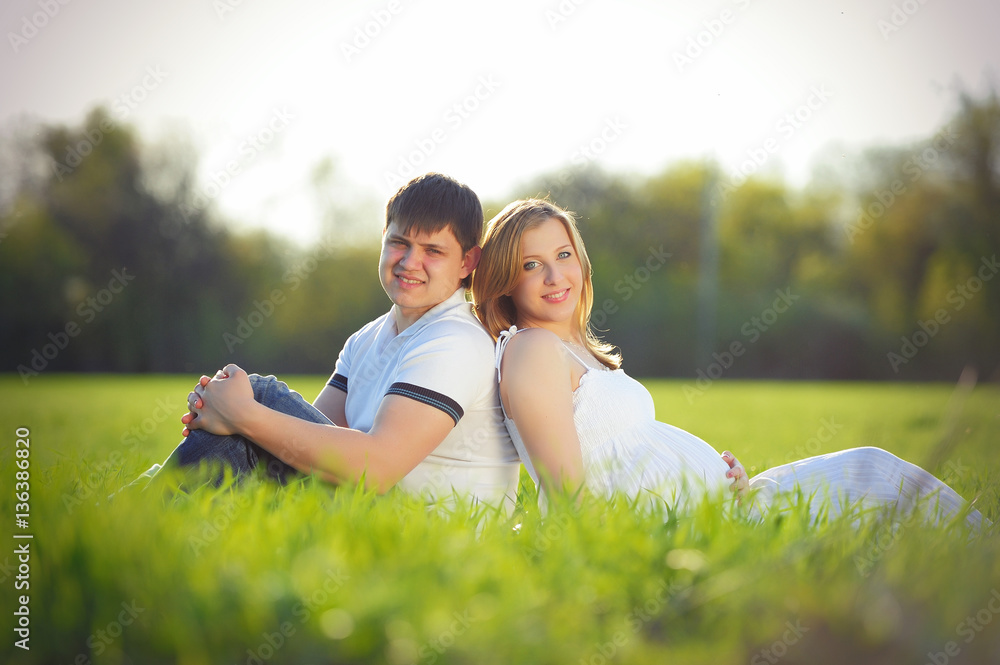young pregnant couple sitting on green grass in spring young pregnant couple sitting on green grass in spring