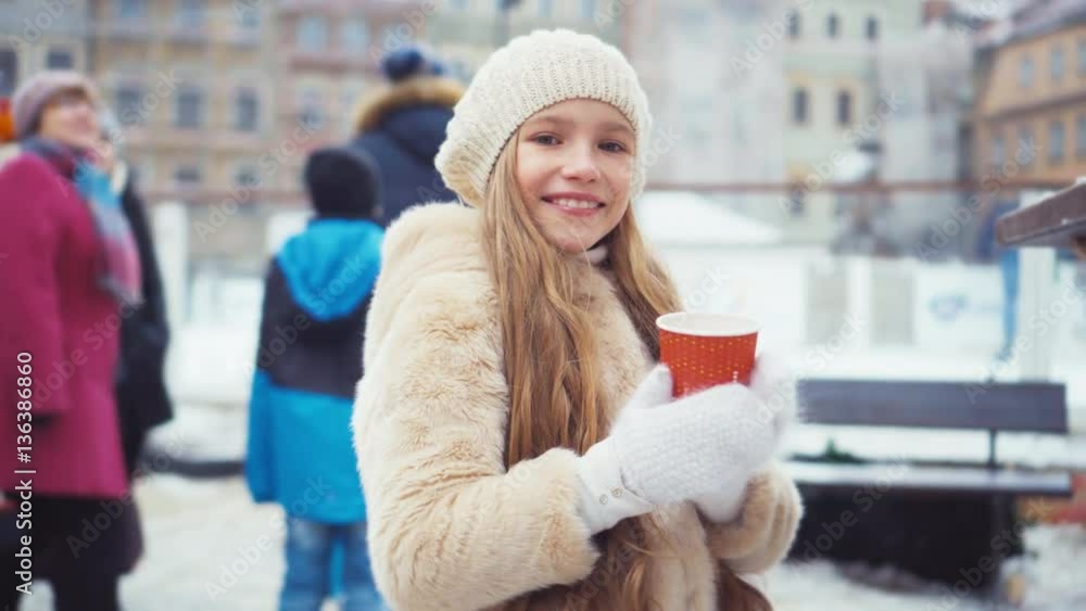 Child 8 years old holds cup of tea outdoors in winter and smiling at camera. Child among the crowd of people Child 8 years old holds cup of tea outdoors in winter and smiling at camera. Child among the crowd of people