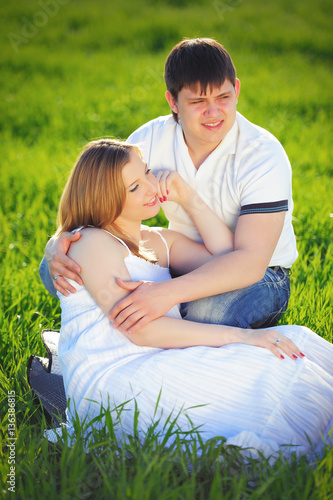 young pregnant couple sitting on green grass in spring © lanarusfoto