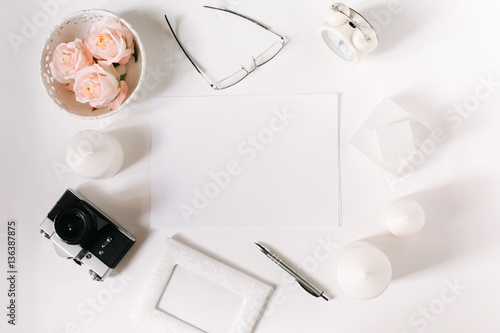 White desk with glasses, roses, candles, pen and film camera. Empty sheet in the middle. Top view, flat lay, copyspace.