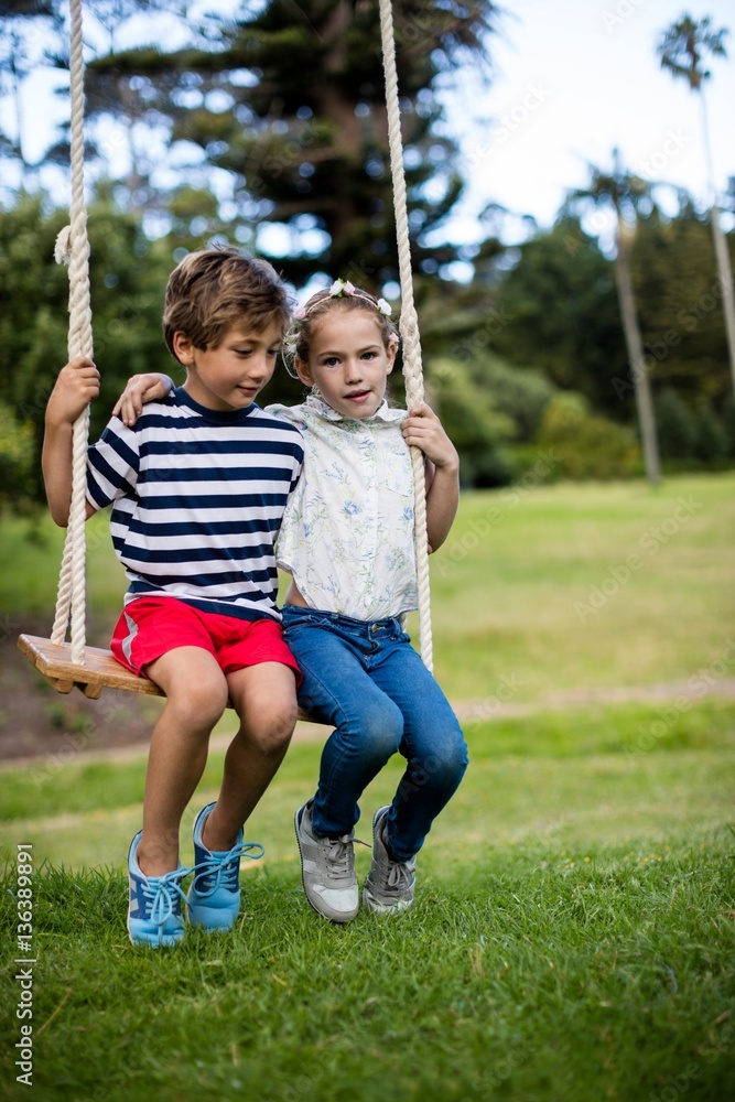 Boy and girl sitting on a swing in park Boy and girl sitting on a swing in park