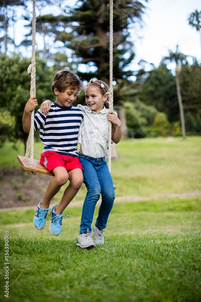 Boy and girl sitting on a swing in park Boy and girl sitting on a swing in park