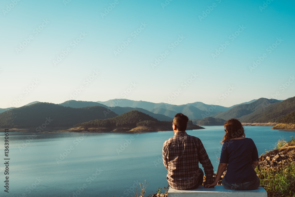 a couple stand hugging, embracing, overlooking a lake with mountains in the background. Traveling together, adventure