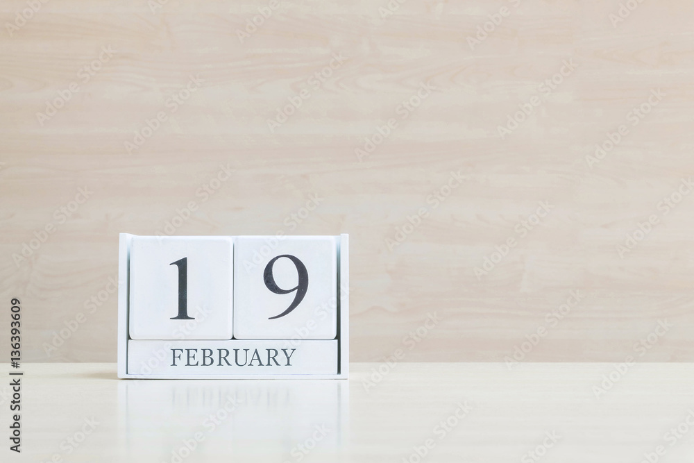 Closeup surface white wooden calendar with black 19 february word on blurred brown wood desk and wood wall textured background with copy space in selective focus at the calendar Closeup surface white wooden calendar with black 19 february word on blurred brown wood desk and wood wall textured background with copy space in selective focus at the calendar