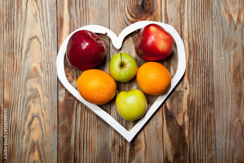 White heart, apples and oranges on the wooden background