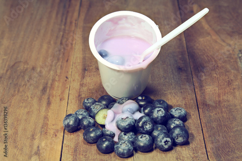 Blueberries with yogurt in a white cup on wooden background.