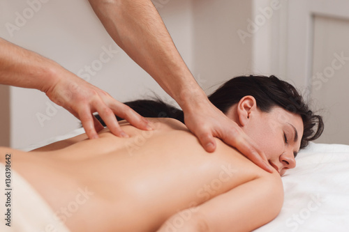 Nude woman enjoying massage, free space. Young dreamy brunette lying on massaging table and relaxing while masseur beating her back. Rest after work, pleasure, spa, body care concept