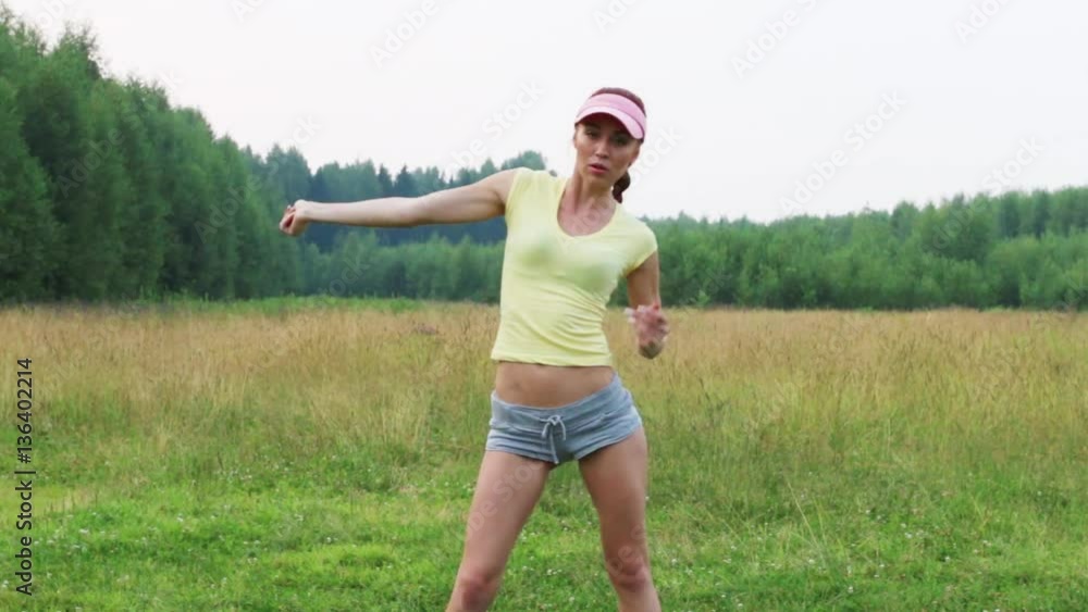 Girl in shorts and cap dances on green meadow at summer evening Girl in shorts and cap dances on green meadow at summer evening