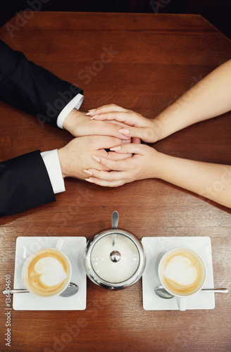 Hands of the newlyweds and two cups of cappuccino