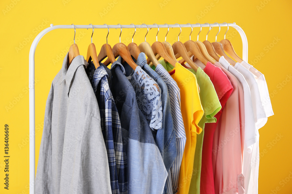 Hangers with colorful clothes on yellow background