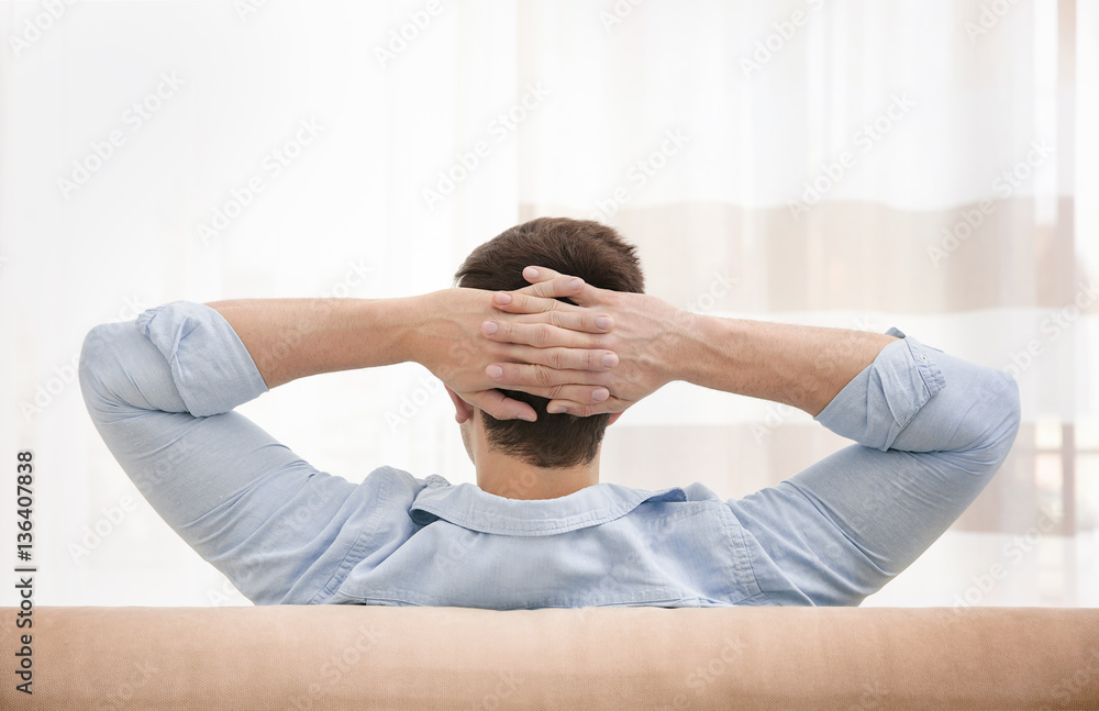 Young man resting on couch with hands behind his head in light room Young man resting on couch with hands behind his head in light room