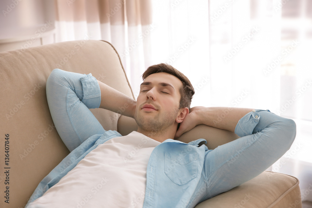 Young man resting on couch with hands behind his head in light room Young man resting on couch with hands behind his head in light room