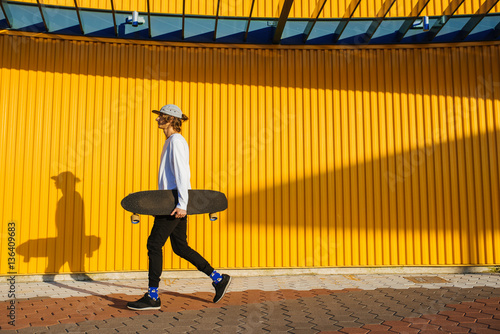 Fototapeta Young skater boy walking outdoors with longboard