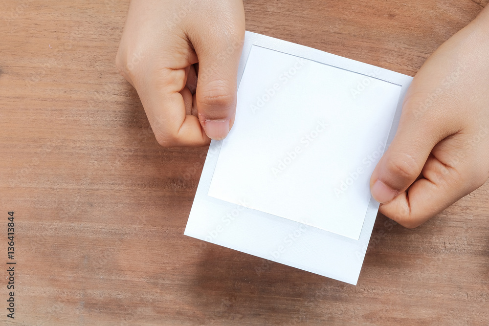 Hand holding a blank photo frame in front of wooden background. Hand holding a blank photo frame in front of wooden background.