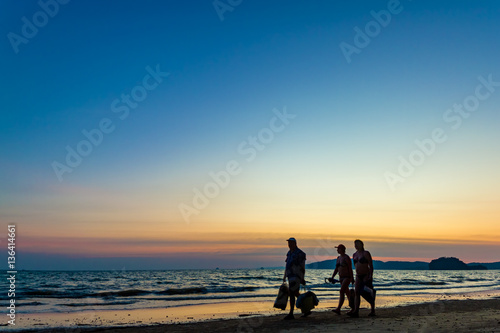 Family of tourists walk along the beach against the backdrop of a beautiful sunset