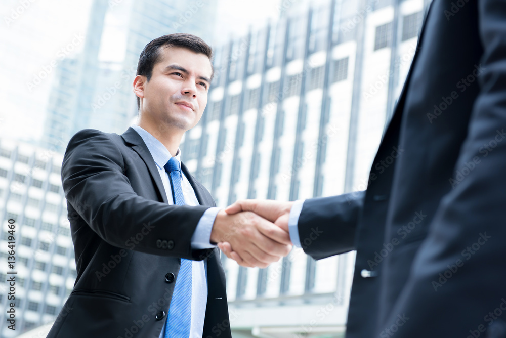 Businessmen making handshake in front of office buildings in the city Businessmen making handshake in front of office buildings in the city