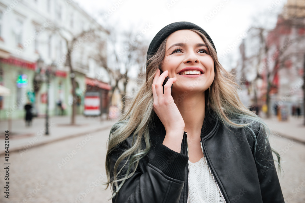Smiling young woman walking and talking by mobile phone.