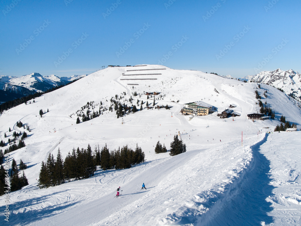 Downhill slope and apres ski mountain hut with restaurant terrace in Saalbach Hinterglemm Leogang winter resort, Tirol, Austria, Europe. Sunny day shot.