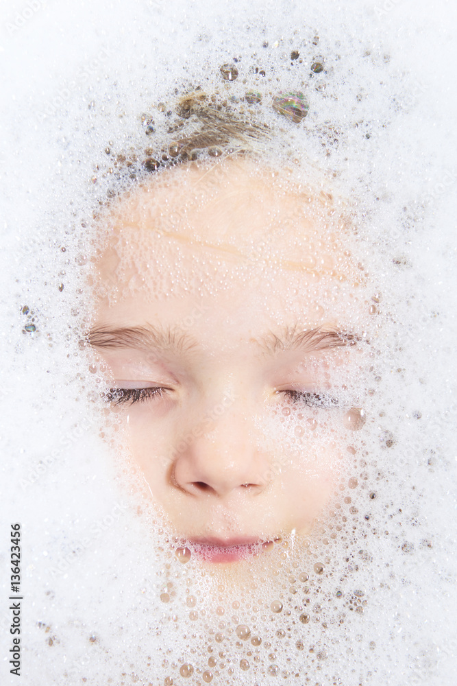 Funny little child blond girl in a bubble bath filled with soap foam