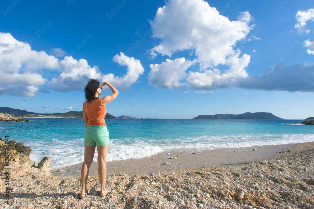 Woman in an orange T-shirt and shorts looking into the distance on the seashore