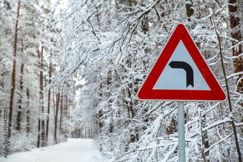Snowy winter road. Forest with snow-covered trees. Beautiful wintertime. Attention sign. Turn to the left.