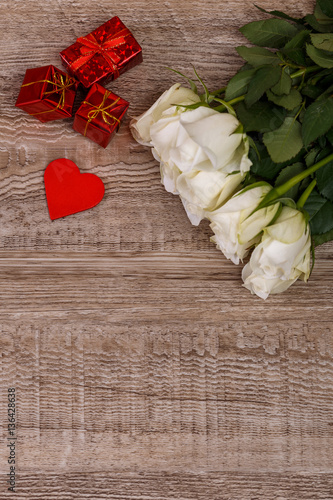 White roses with heart on wood background. Love design. 8 march concept. Fresh natural flowers with gift boxes. Wooden rustic board.