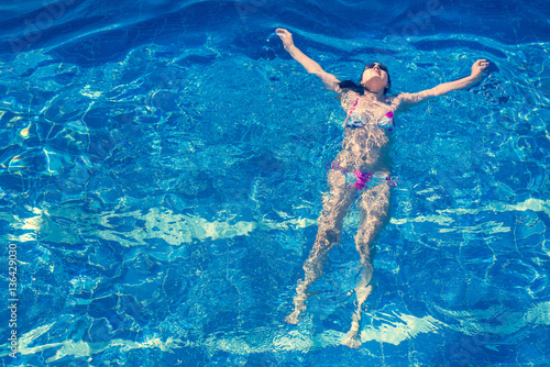 Woman in bikini and sunglasses swims in the pool