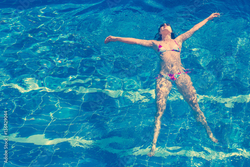 Woman in bikini and sunglasses  swims in the pool