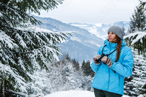 Portrait of young woman with binoculars in hand on the background of winter mountains