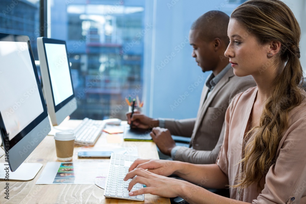 Graphic designer working at desk with colleague Graphic designer working at desk with colleague